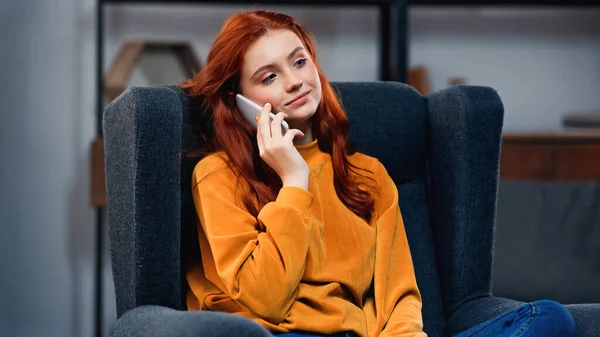 Smiling girl talking on smartphone on armchair — Stock Photo