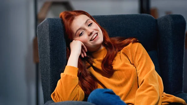 Adolescent aux cheveux rouges souriant assis sur un fauteuil — Photo de stock