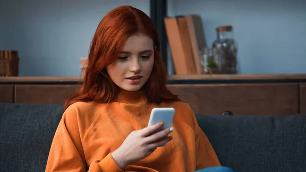 Fille aux cheveux rouges utilisant un smartphone sur le canapé — Photo de stock