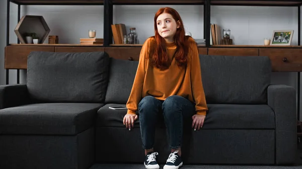 Triste adolescente dai capelli rossi seduto vicino al cellulare sul divano — Foto stock
