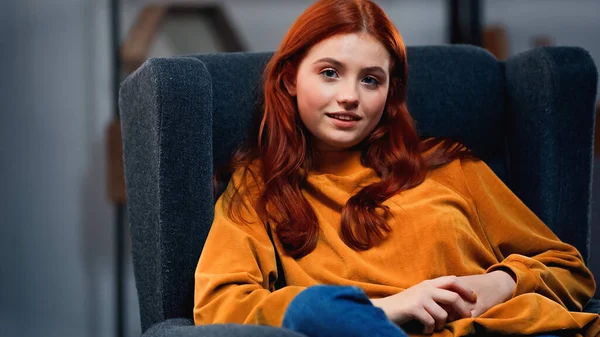 Adolescent aux cheveux rouges souriant à la caméra sur un fauteuil — Photo de stock