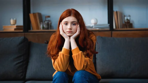 Vermelho adolescente de cabelos olhando para a câmera enquanto sentado no sofá em casa — Fotografia de Stock