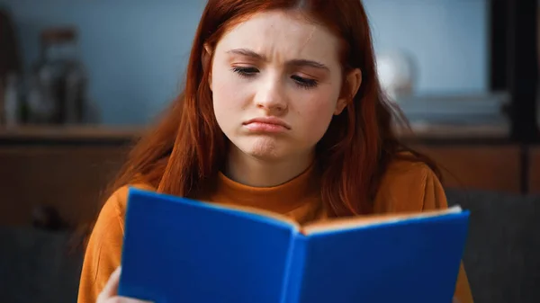Trauriges Mädchen liest Buch auf verschwommenem Vordergrund — Stockfoto