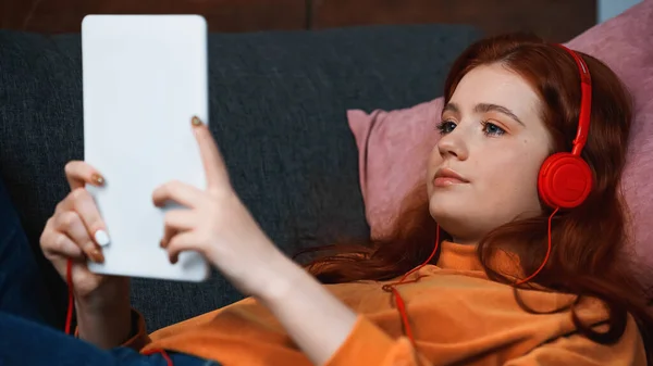 Adolescente em fones de ouvido usando tablet digital em primeiro plano desfocado — Fotografia de Stock