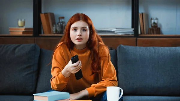 Menina com controle remoto sentado perto de copo e livro — Fotografia de Stock