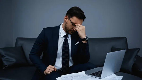 Müder Geschäftsmann sitzt neben Laptop und Papieren im Hotelzimmer — Stockfoto