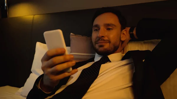 Businessman using smartphone on blurred foreground on hotel bed — Stock Photo