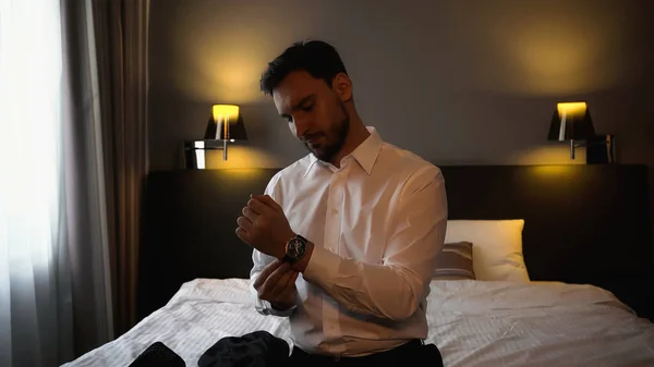 Businessman wearing wristwatch near bed in hotel room — Stock Photo