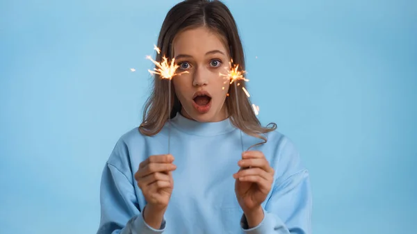 Shocked teenage girl in soft sweatshirt holding sparklers isolated on blue — Stock Photo