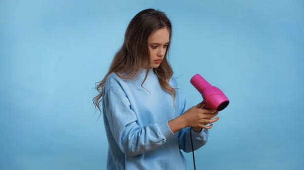 Teenager Mädchen in weichem Sweatshirt mit rosa Haartrockner isoliert auf blau — Stockfoto