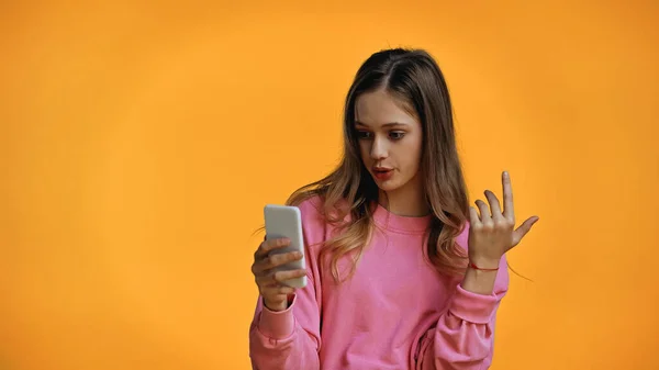 Adolescente en sudadera rosa mirando teléfono inteligente aislado en amarillo - foto de stock