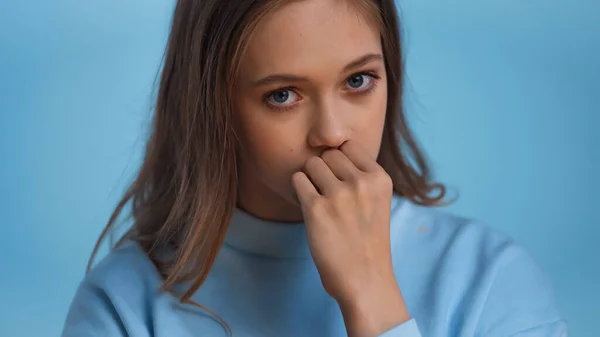 Worried teenage girl in sweatshirt looking at camera isolated on blue — Stock Photo