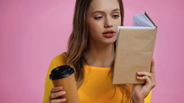 Adolescente leyendo libro y sosteniendo café para ir aislado en rosa - foto de stock