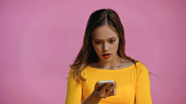 Chocado adolescente mirando teléfono inteligente aislado en rosa - foto de stock