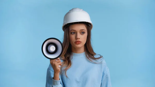 Teenage girl in hard hat holding megaphone isolated on blue — Stock Photo