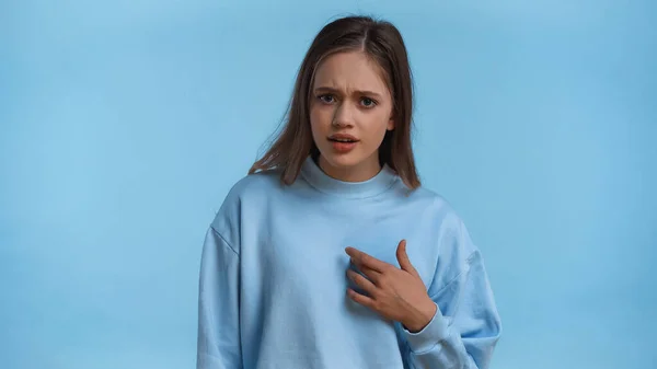 Dissatisfied teenage girl in sweatshirt pointing at herself isolated on blue — Stock Photo