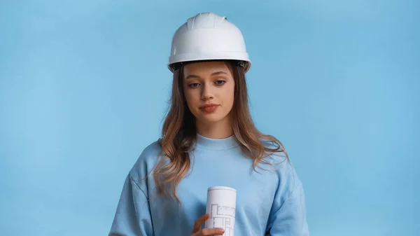 Teenage girl in hard hat holding rolled blueprint isolated on blue — Stock Photo