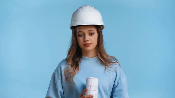 Adolescente em chapéu duro segurando rolou planta isolada em azul — Fotografia de Stock