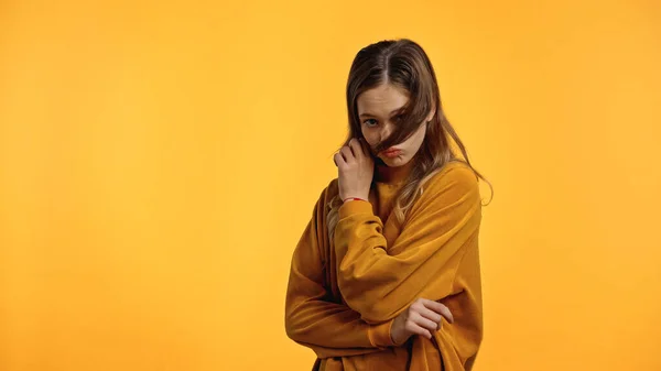 Teenager in sweater with pouting lips looking at camera while adjusting hair isolated on yellow — Stock Photo