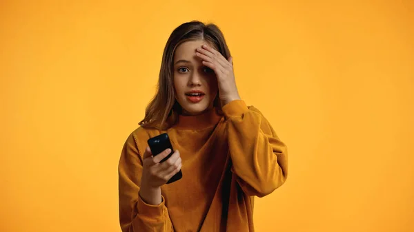 Amazed teenager in sweater holding remote controller isolated on yellow — Stock Photo