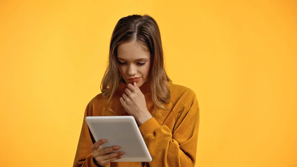 Pensive teenager in sweater looking at digital tablet isolated on yellow — Stock Photo