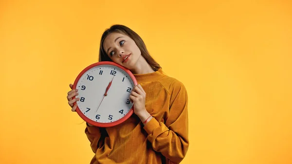 Smiling teenager in sweater holding clock isolated on yellow — Stock Photo