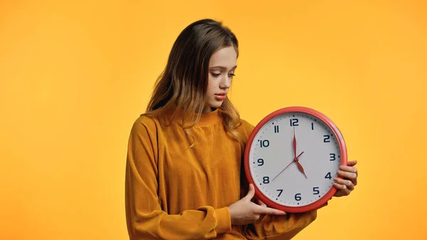 Teenage girl in sweater looking at clock isolated on yellow — Stock Photo