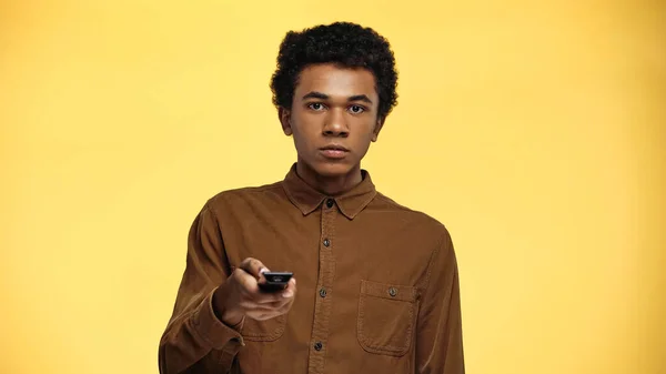 Curly african american teenage boy holding remote controller isolated on yellow — Stock Photo