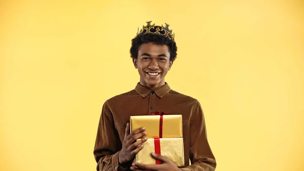 Afro-americano adolescente em coroa sorrindo enquanto segurando presentes isolados no amarelo — Fotografia de Stock