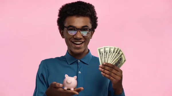 Africano americano adolescente segurando dólares e porquinho banco isolado em rosa — Fotografia de Stock