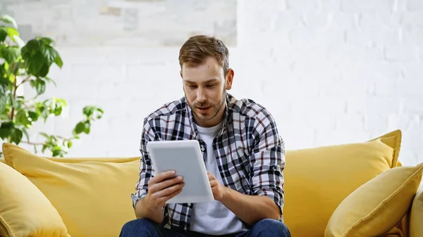 Bärtiger Mann im karierten Hemd mit digitalem Tablet im Wohnzimmer — Stockfoto