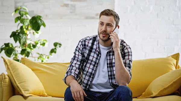 Бородатый мужчина разговаривает на смартфоне, сидя на диване — стоковое фото
