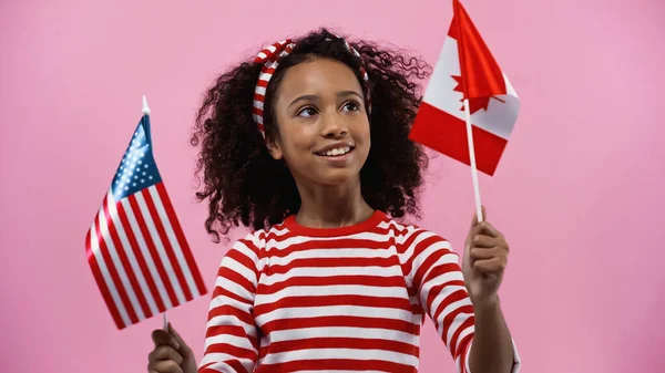 Joyeuse fille afro-américaine tenant des drapeaux d'Amérique et du canada isolés en rose — Photo de stock