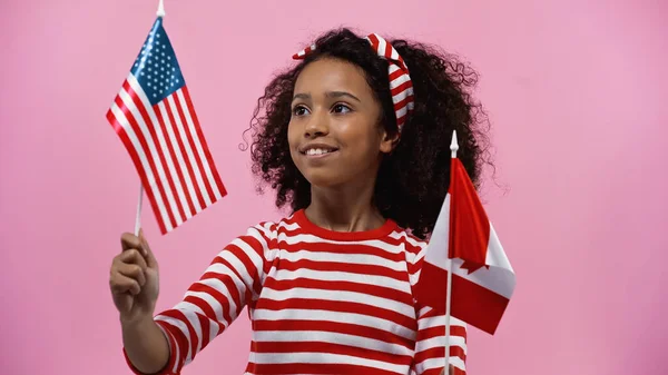 Souriante fille afro-américaine tenant des drapeaux d'Amérique et du canada isolés en rose — Photo de stock