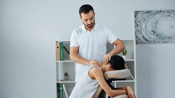 Masseur doing neck massage to businesswoman on massage chair in office — Stock Photo