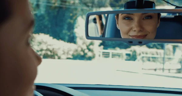 Happy woman smiling and looking in rearview mirror of car — Stock Photo