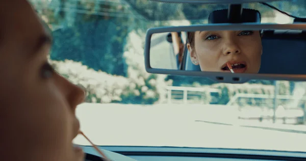 Blurred and happy woman applying lip gloss and looking in rearview mirror — Stock Photo