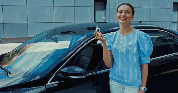 Щаслива молода жінка тримає ключ від автомобіля біля нового автомобіля — стокове фото