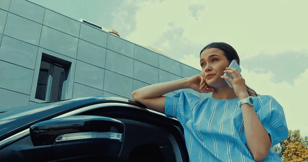 Blick auf junge Frau, die sich auf Auto lehnt, während sie mit dem Smartphone spricht — Stockfoto