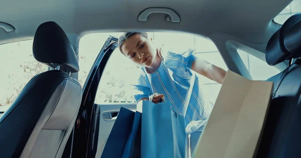 Jeune femme prenant des sacs à provisions sur le siège arrière de la voiture — Photo de stock