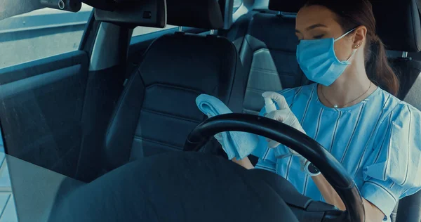 Woman in medical mask spraying sanitizer on rag inside of car — Stock Photo