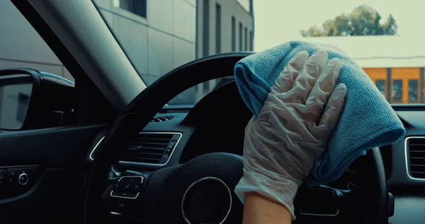 Cropped view of woman in latex glove disinfecting steering wheel with rag — Stock Photo