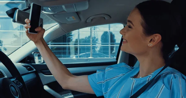 Vue latérale de la femme heureuse prenant selfie sur smartphone à l'intérieur de la voiture — Photo de stock