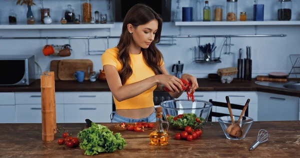 Junge Frau fügt Paprika in Schüssel mit Salat hinzu — Stockfoto