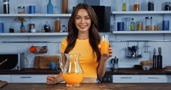 Fröhliche junge Frau mit Krug mit Orangensaft und Glas — Stockfoto