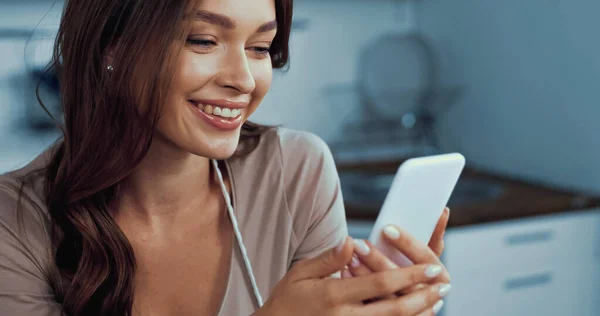 Mujer joven feliz usando el teléfono inteligente en la cocina - foto de stock