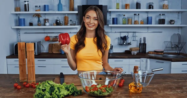Happy woman holding fresh bell pepper near ingredients on table — Stock Photo