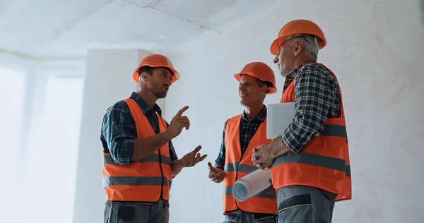 Builder gesturing while talking with coworkers on construction site — Stock Photo