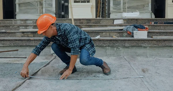 Builder measuring ground with industrial measuring tape on construction site — Stock Photo