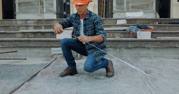 Mature builder measuring ground with industrial measuring tape on construction site — Stock Photo